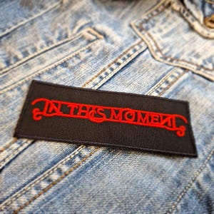 Könnte beinhalten: Schwarzer Stoff-Patch mit den Worten "In This Moment" in roter Stickerei.