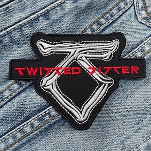 Può includere: Una toppa ricamata in bianco e nero con il testo "TWISTED SISTER" in lettere rosse. La toppa è cucita su un tessuto di jeans blu.