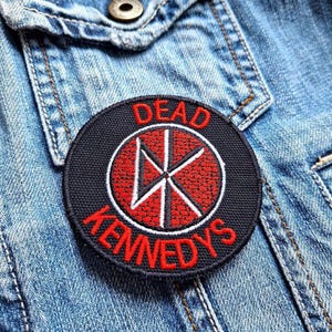 Op de afbeelding: Een geborduurde zwarte en rode patch met de tekst "DEAD KENNEDYS" en een rood en wit symbool.
