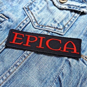 Könnte beinhalten: Schwarzer und roter gestickter Aufnäher mit dem Wort "EPICA" in roten Buchstaben.