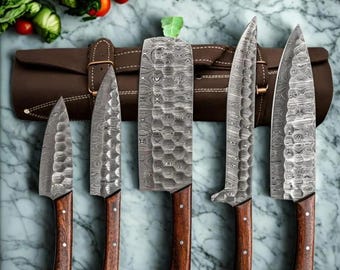 May include: Set of five kitchen knives with Damascus steel blades and wooden handles. The knives are arranged in a leather roll with a brown background.