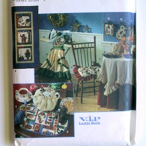 Puede incluir: Sobre de patrón de costura Simplicity 7709 Home Decorating con ilustraciones de un delantal con volantes, cojín para silla, mantel, funda para tetera y tapiz. El paquete muestra varios proyectos de tela con motivos de osos y flores.
