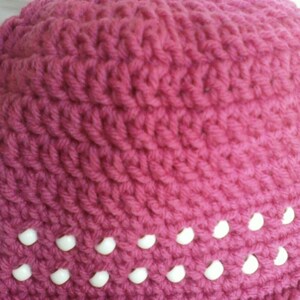 May include: A pink crocheted hat with a row of white beads around the bottom edge.