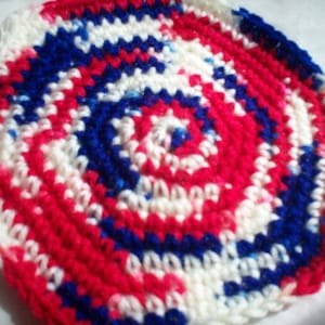 May include: A crocheted round coaster with a spiral pattern in red, white, and blue.