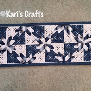 May include: A crocheted runner with a geometric pattern in navy blue and pink. The runner is made with a simple stitch and has a clean, modern look.