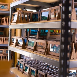 May include: A shelf unit filled with wooden frames containing sand art. The frames are arranged in rows and are all the same size. The sand art is a variety of colors and designs.