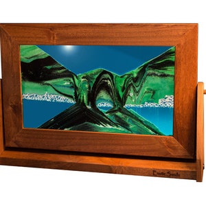 May include: A wooden framed sand art piece with a blue and green sand design. The frame has a stand and the words "Exotic Sands" are printed on the bottom.