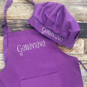 May include: Purple chef's apron and hat set with the name "Genevieve" embroidered on both pieces.