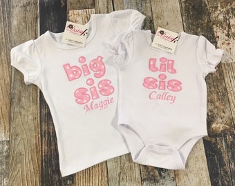 May include: Two white t-shirts with pink polka dot lettering. One shirt says "big sis Maggie" and the other says "lil sis Calley".