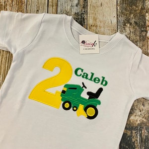 May include: White t-shirt with a yellow number 2 and a green tractor with the name Caleb embroidered on it.