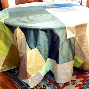 May include: A patchwork tablecloth with a geometric design in shades of green, brown, and gold. The tablecloth is made of a silky fabric and has a luxurious feel.