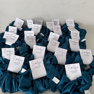 May include: Teal satin scrunchies with white labels that say "Emily's Hens Party 25-05-24".