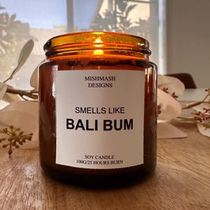 K&ouml;nnte beinhalten: Eine braune Glaskerze in einem Glas mit einem wei&szlig;en Etikett, auf dem "Mishmash Designs" und "Smells Like Bali Bum" steht. Das Etikett tr&auml;gt au&szlig;erdem die Aufschrift "Soy Candle 100g/25 Hours Burn".