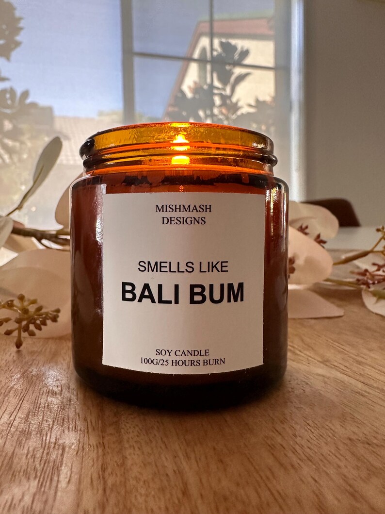 K&ouml;nnte beinhalten: Eine braune Glaskerze in einem Glas mit einem wei&szlig;en Etikett, auf dem "Mishmash Designs" und "Smells Like Bali Bum" steht. Das Etikett tr&auml;gt au&szlig;erdem die Aufschrift "Soy Candle 100g/25 Hours Burn".