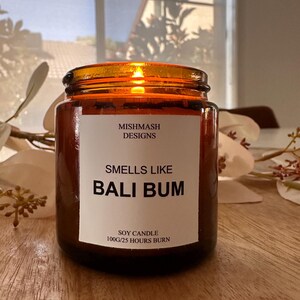 K&ouml;nnte beinhalten: Eine braune Glas-Sojawachskerze mit einem wei&szlig;en Etikett, auf dem "Mishmash Designs" und "Smells Like Bali Bum" steht. Das Etikett tr&auml;gt au&szlig;erdem die Aufschrift "Soy Candle 100g/25 Hours Burn".