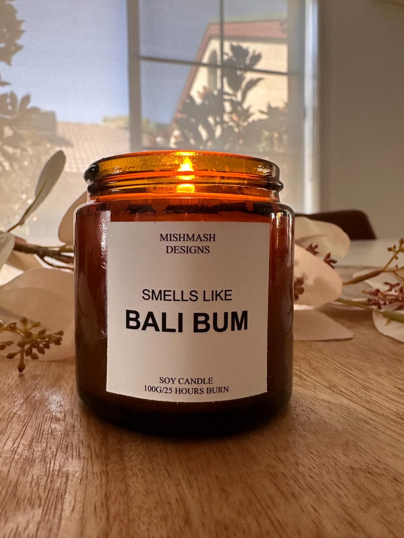 K&ouml;nnte beinhalten: Eine braune Glas-Sojawachskerze mit einem wei&szlig;en Etikett, auf dem "Mishmash Designs" und "Smells Like Bali Bum" steht. Das Etikett tr&auml;gt au&szlig;erdem die Aufschrift "Soy Candle 100g/25 Hours Burn".