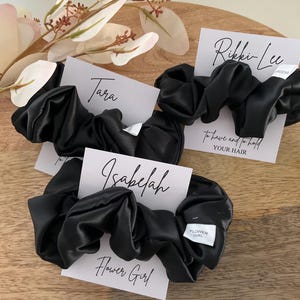 May include: Three black satin hair scrunchies with white cards attached. The cards have the names "Tara", "Isabelah Flower Girl", and "Rikki-Lee" with the text "to have and to hold your hair".