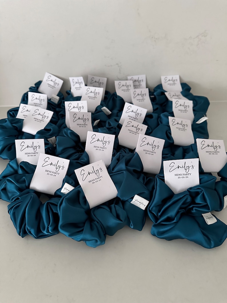 May include: Teal blue satin scrunchies with white tags that say "Emily's Hens Party 25-05-24".
