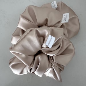 May include: Two satin hair scrunchies in a light beige color. One scrunchie has a tag that says "Bridesmaid" and the other says "Maid of Honor".