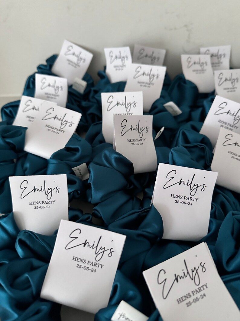 May include: Teal blue satin scrunchies with white labels that say "Emily's Hens Party 25-05-24".