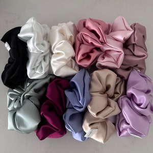 May include: A collection of 10 colorful satin scrunchies in various shades of pink, purple, blue, green, and brown. The scrunchies are arranged in a pile on a white surface.