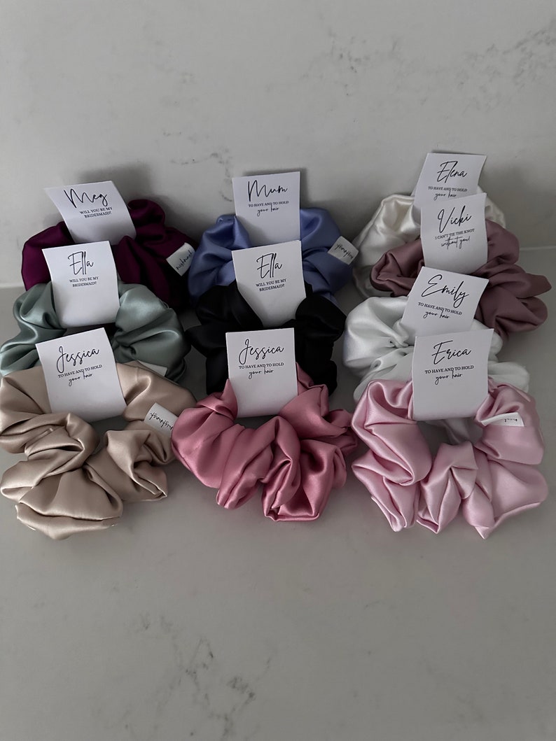 May include: Assortment of satin scrunchies in various colors, each with a personalized card attached. The cards feature different names and messages, such as "Mum", "Ella", "Jessica", and "Erica".