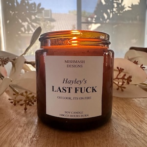 May include: A lit soy candle in a brown glass jar. The label reads "Hayley's LAST FUCK" with the text "OH LOOK, ITS ON FIRE". The candle is 100g and has a 25-hour burn time. The brand name is Mishmash Designs.