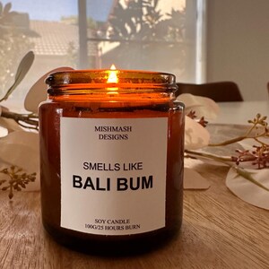K&ouml;nnte beinhalten: Ein braunes Glasgef&auml;&szlig; mit einer Kerze und einem wei&szlig;en Etikett mit der Aufschrift "Mishmash Designs" und "Smells Like Bali Bum". Das Etikett tr&auml;gt au&szlig;erdem die Aufschrift "Soy Candle 100g/25 Hours Burn".