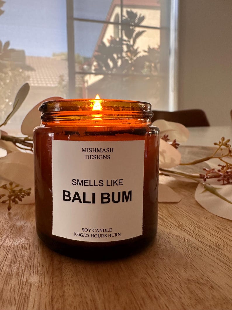 K&ouml;nnte beinhalten: Ein braunes Glasgef&auml;&szlig; mit einer Kerze und einem wei&szlig;en Etikett mit der Aufschrift "Mishmash Designs" und "Smells Like Bali Bum". Das Etikett tr&auml;gt au&szlig;erdem die Aufschrift "Soy Candle 100g/25 Hours Burn".