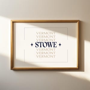 May include: A framed print with a gold-colored frame. The print features the word "STOWE" in navy blue, centered within a white background, with the word "VERMONT" repeated in a gold color above and below.