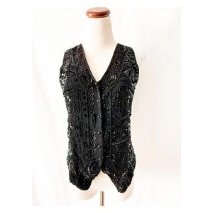May include: A black sequined vest with a geometric pattern. The vest has a V-neck and a button closure.
