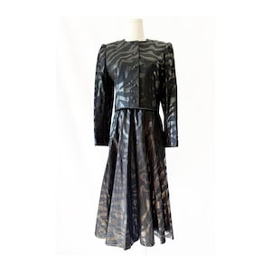 May include: A black two-piece outfit featuring a jacket and a midi skirt. The jacket has long sleeves and a button-up front. The skirt is a-line. Both pieces have a zebra stripe pattern.