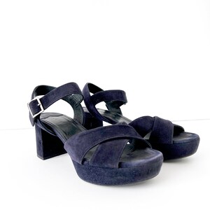 Op de afbeelding: Een paar donkerblauwe su&egrave;de platform sandalen met een gespsluiting. De sandalen hebben een dik platform en een chunky hak.
