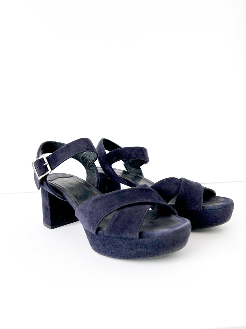 Op de afbeelding: Een paar donkerblauwe su&egrave;de platform sandalen met een gespsluiting. De sandalen hebben een dik platform en een chunky hak.