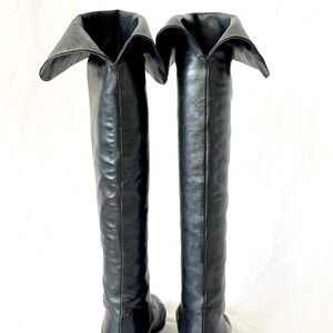 May include: A pair of black leather knee-high boots with a folded-over top. The boots have a pointed toe and a low heel.
