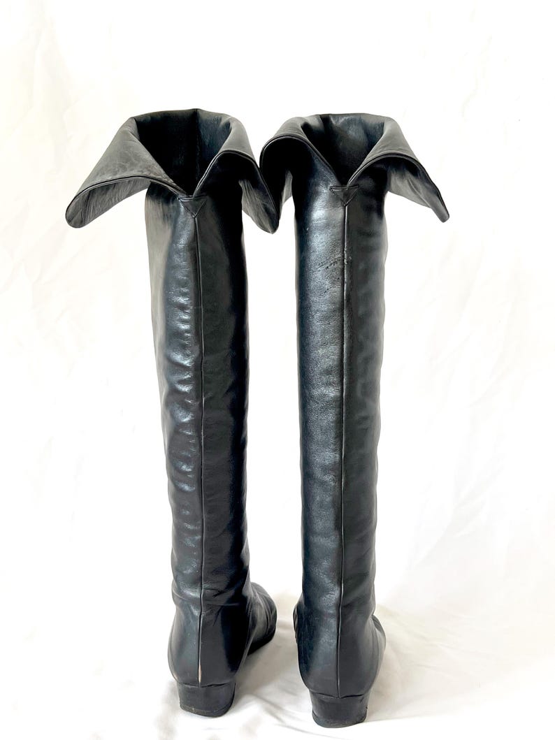 May include: A pair of black leather knee-high boots with a folded-over top. The boots have a pointed toe and a low heel.