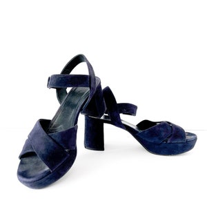 Op de afbeelding: Een paar donkerblauwe su&egrave;de plateau sandalen met enkelbandjes. De sandalen hebben een dikke hak en een gekruist bandje ontwerp.