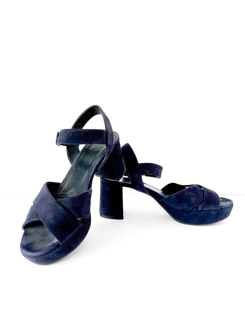 Op de afbeelding: Een paar donkerblauwe su&egrave;de plateau sandalen met enkelbandjes. De sandalen hebben een dikke hak en een gekruist bandje ontwerp.