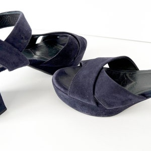 Op de afbeelding: Een paar donkerblauwe su&egrave;de sandalen met een gekruiste band.