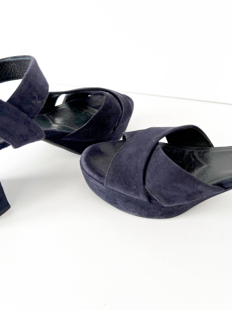 Op de afbeelding: Een paar donkerblauwe su&egrave;de sandalen met een gekruiste band.