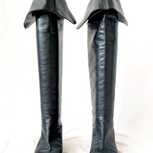 May include: A pair of black leather knee-high boots with a folded-over top. The boots have a pointed toe and a low heel.