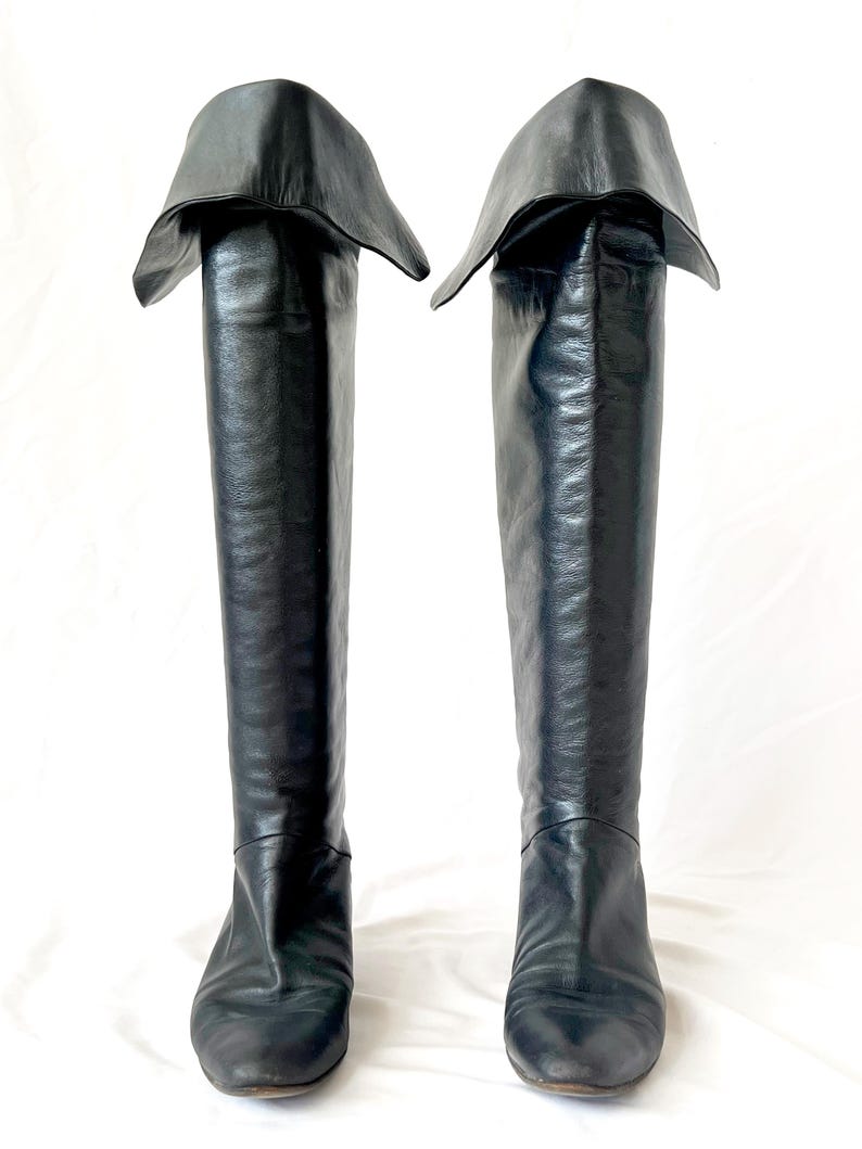 May include: A pair of black leather knee-high boots with a folded-over top. The boots have a pointed toe and a low heel.