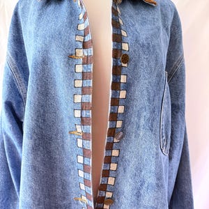 May include: Light blue denim jacket with a brown corduroy collar. The jacket features a checkered pattern in brown and white along the front edges and gold-colored buttons. A classic denim jacket.