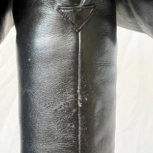 May include: Close-up of a black leather boot with a seam down the back. The boot has a pointed toe and a triangular detail at the top.