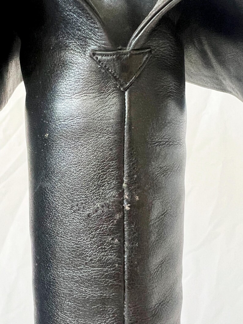 May include: Close-up of a black leather boot with a seam down the back. The boot has a pointed toe and a triangular detail at the top.