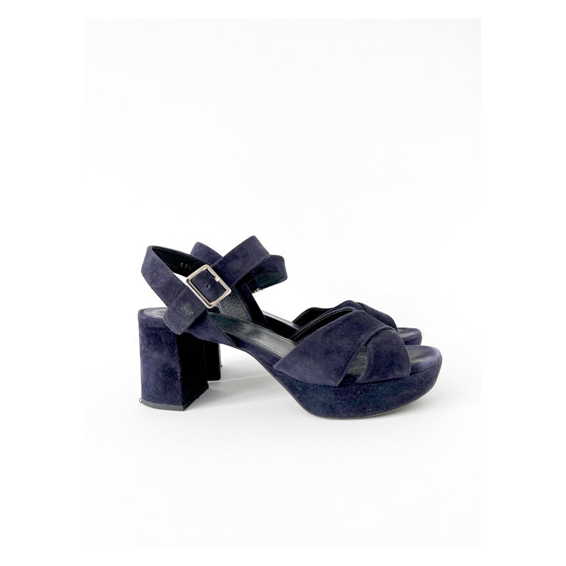 Op de afbeelding: Donkerblauwe su&egrave;de plateau sandalen met een gespsluiting aan de enkel en een blokhak.