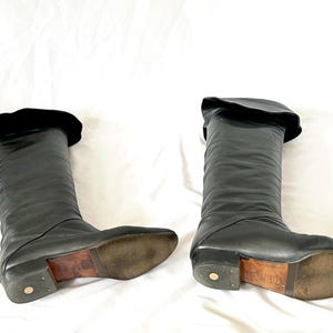 May include: A pair of black leather knee-high boots with a fold-over top. The boots have a pointed toe and a low heel.