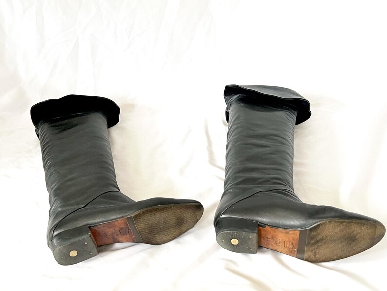 May include: A pair of black leather knee-high boots with a fold-over top. The boots have a pointed toe and a low heel.