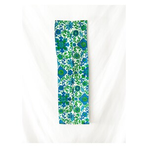 May include: A long, narrow fabric panel with a white background and a repeating pattern of blue and green flowers. The fabric is perfect for crafting projects, like making a table runner or a pillow cover.