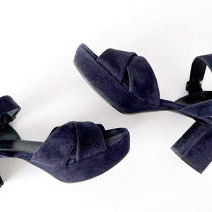 Op de afbeelding: Een paar donkerblauwe su&egrave;de plateau sandalen met enkelbandjes. De sandalen hebben een dikke hak en een gekruist bandje ontwerp.